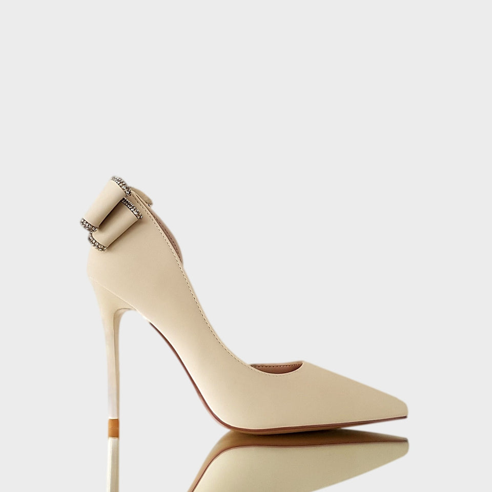 Stilettos en color blanco crema con detalle de moño bordeado en strass en el talón y taco de acrílico al tono de 10.5 cm de altura