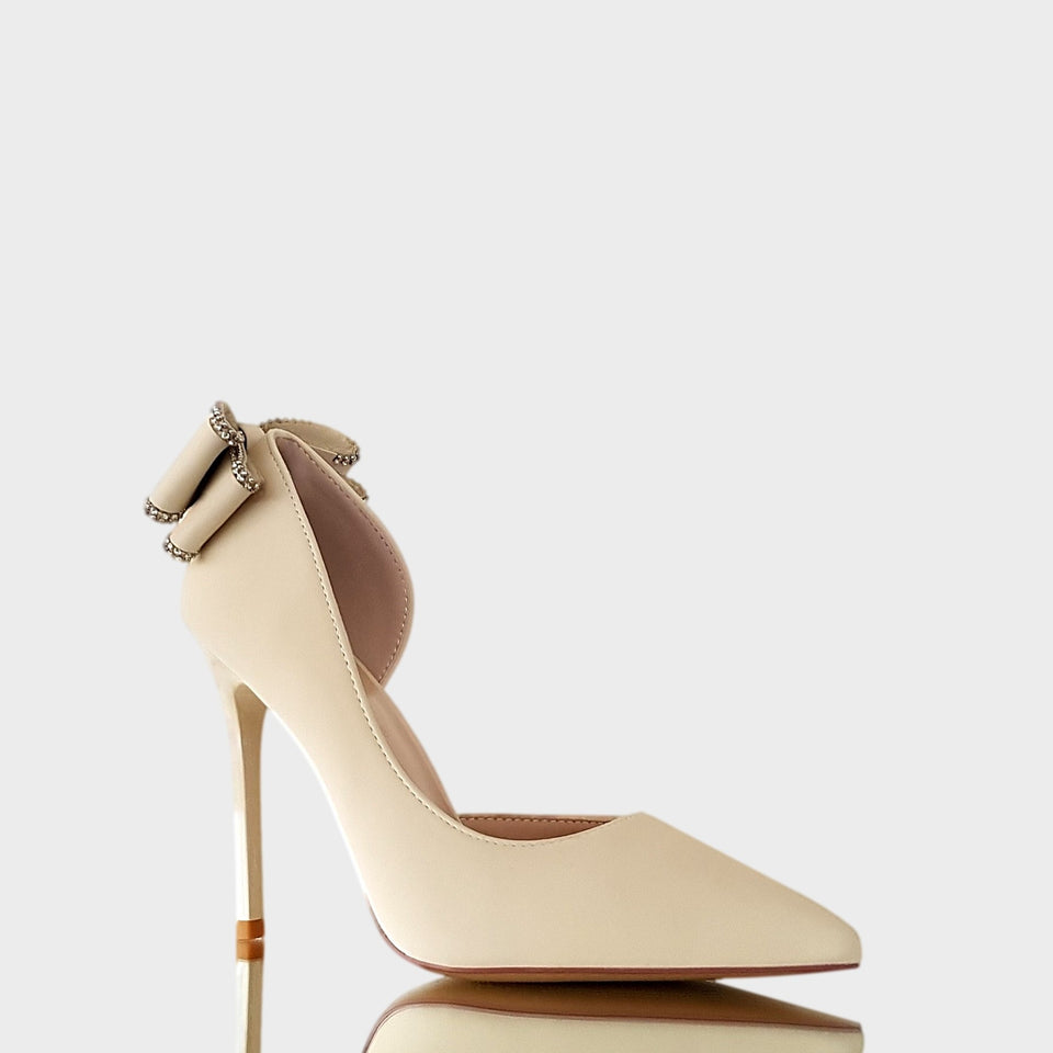 Vista lateral de stilettos en color blanco crema con detalle de moño bordeado en strass en el talón y taco de acrílico al tono de 10.5 cm de altura