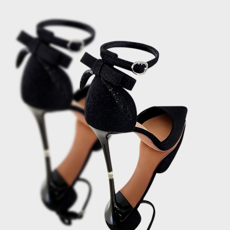 La chica de los stilettos Vista Lateral de Par de Stilettos Samy Black en Cuero PU con Acabado Brillante Moño en el Talón Pulsera al Tobillo y Taco Acrílico Negro de 10 cm 