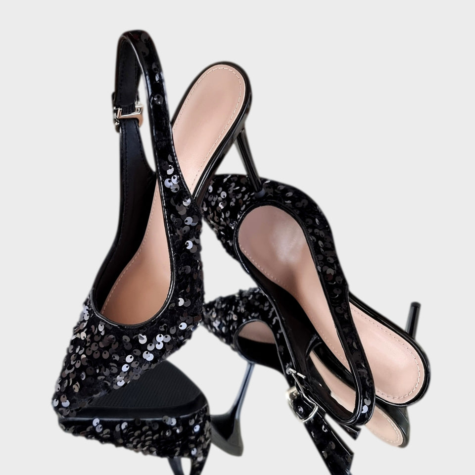 Par de elegantes stilettos de fiesta en lentejuelas de color negro, con talón descubierto y finísimo taco acrílico al tono de 10 cm