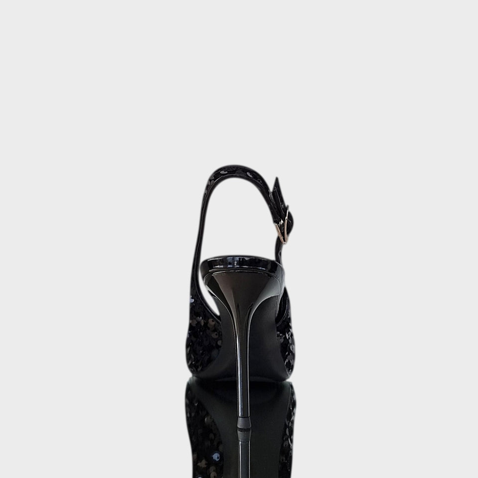 Vista de talón y taco de elegantes stilettos de fiesta en lentejuelas de color negro, con talón descubierto y finísimo taco acrílico al tono de 10 cm