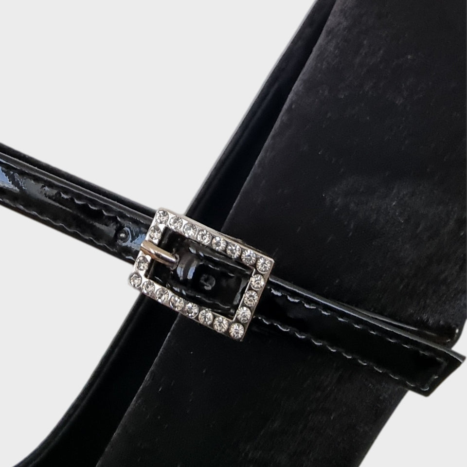 Vista en detalle de la hebilla de los Zapatos Emma Black, de estilo francés, en materail satinado negro, con taco bloque de acrílico al tono de 5 cm, y correa de charol que se ajusta  al empeine con una delicada hebilla de strass