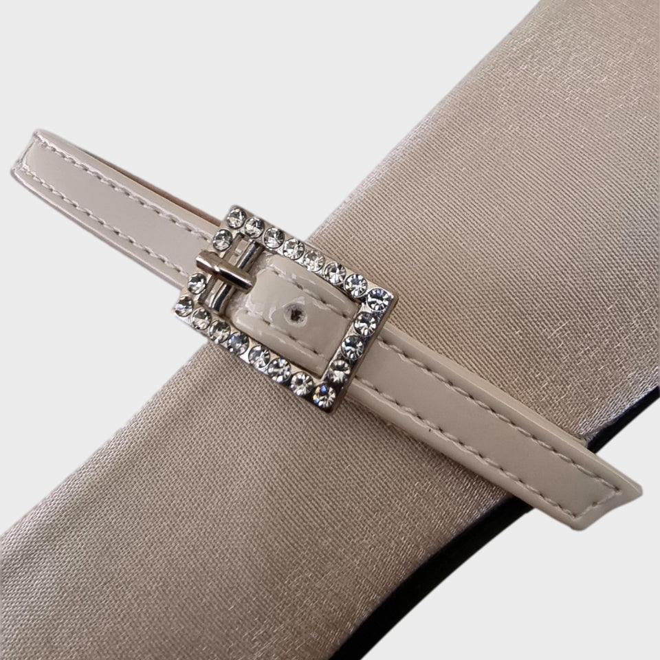 Vista en detalle de hebilla de los Zapatos Emma Champagne, de estilo francés, en materail satinado natural, con taco bloque de acrílico al tono de 5 cm, y correa de charol que se ajusta  al empeine con una delicada hebilla de strass